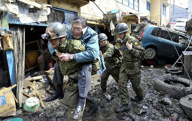 A member of Japan’s Self Defence Force carries a man through a street strewn with debris