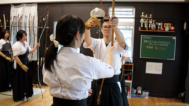 A student showing a man how to hold a bow in kyudo