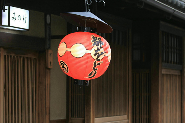 A red paper lantern with Miyako Odori written on it, in front of a wooden building in Gion