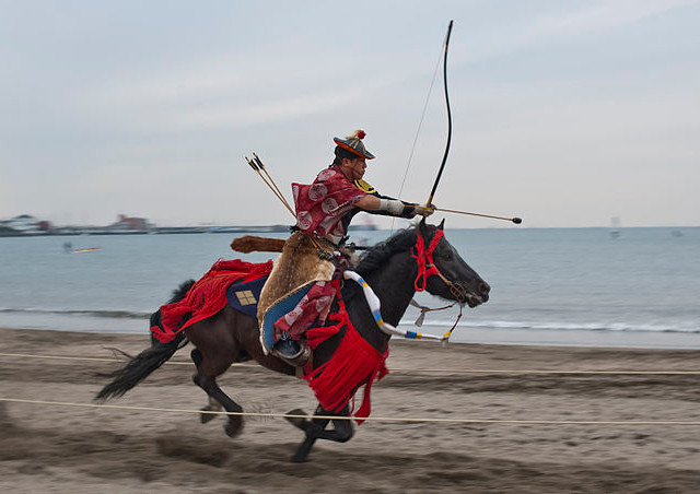 A horse carrying a man about to shoot an arrow from a bow gallops on the beach in Zushi, Japan