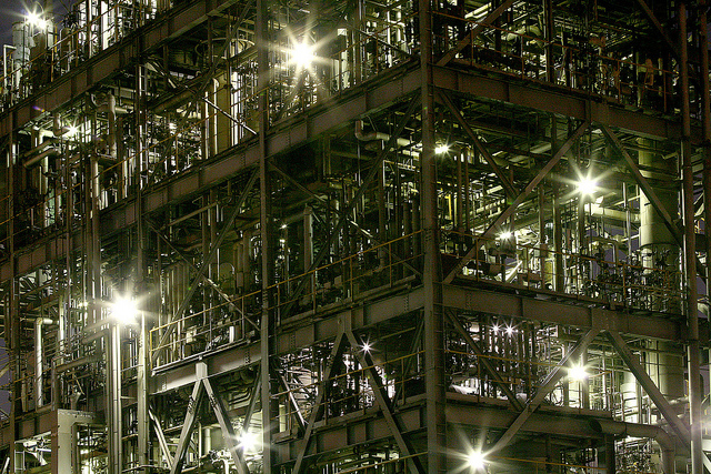 A complex metal structure of struts and pipes, illuminated from within by bright lights