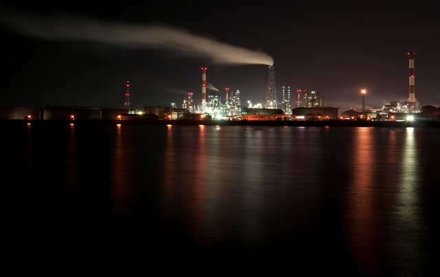 Reflections from factory lights illuminate the surface of the sea at night