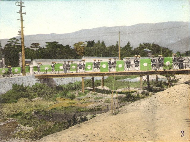 A line of porters carrying possesions across a bridge in Japan