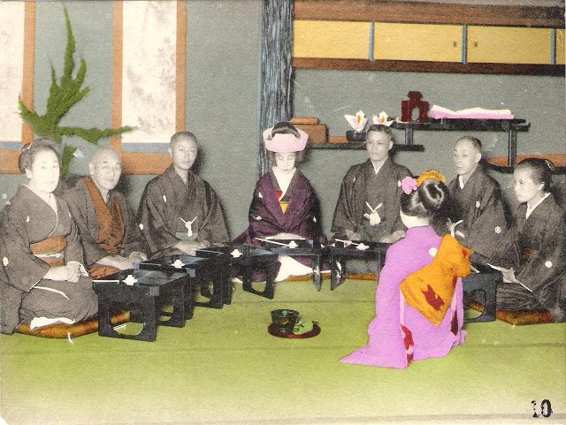 A Japanese bride and groom surrounded by their families, all kneeling on cushions in front of low tables