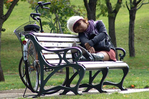 A young woman sleeps on a bench in a park